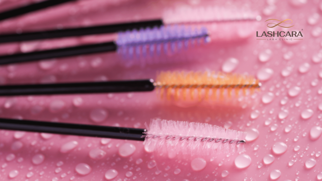 Clean disposable lash brushes arranged on a pink surface with water droplets for a professional lash service at Lashcara.